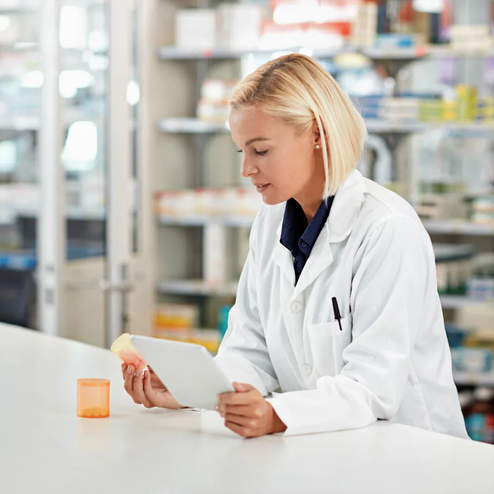 Pharmacist using a tablet to verify medication details with prescription management for pharmacies, improving pharmacy prescription management accuracy and efficiency.