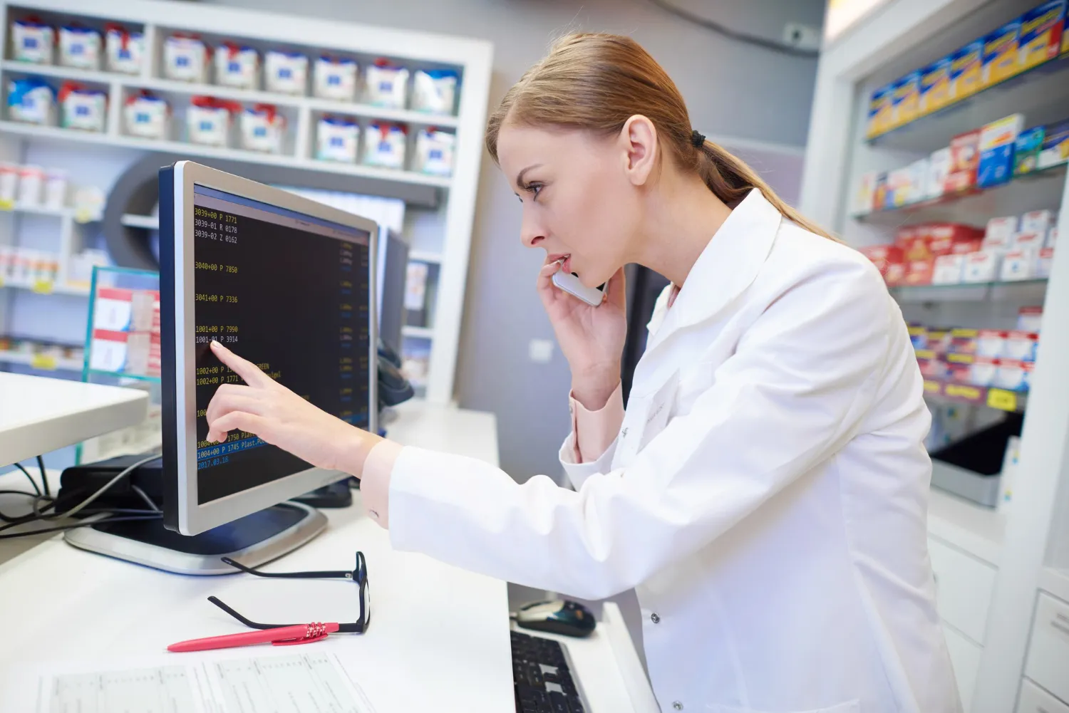 Pharmacist reviewing medication data on a computer while speaking on the phone, representing Prior Authorization Processing for Pharmacies to ensure timely approval and reduce prescription delays