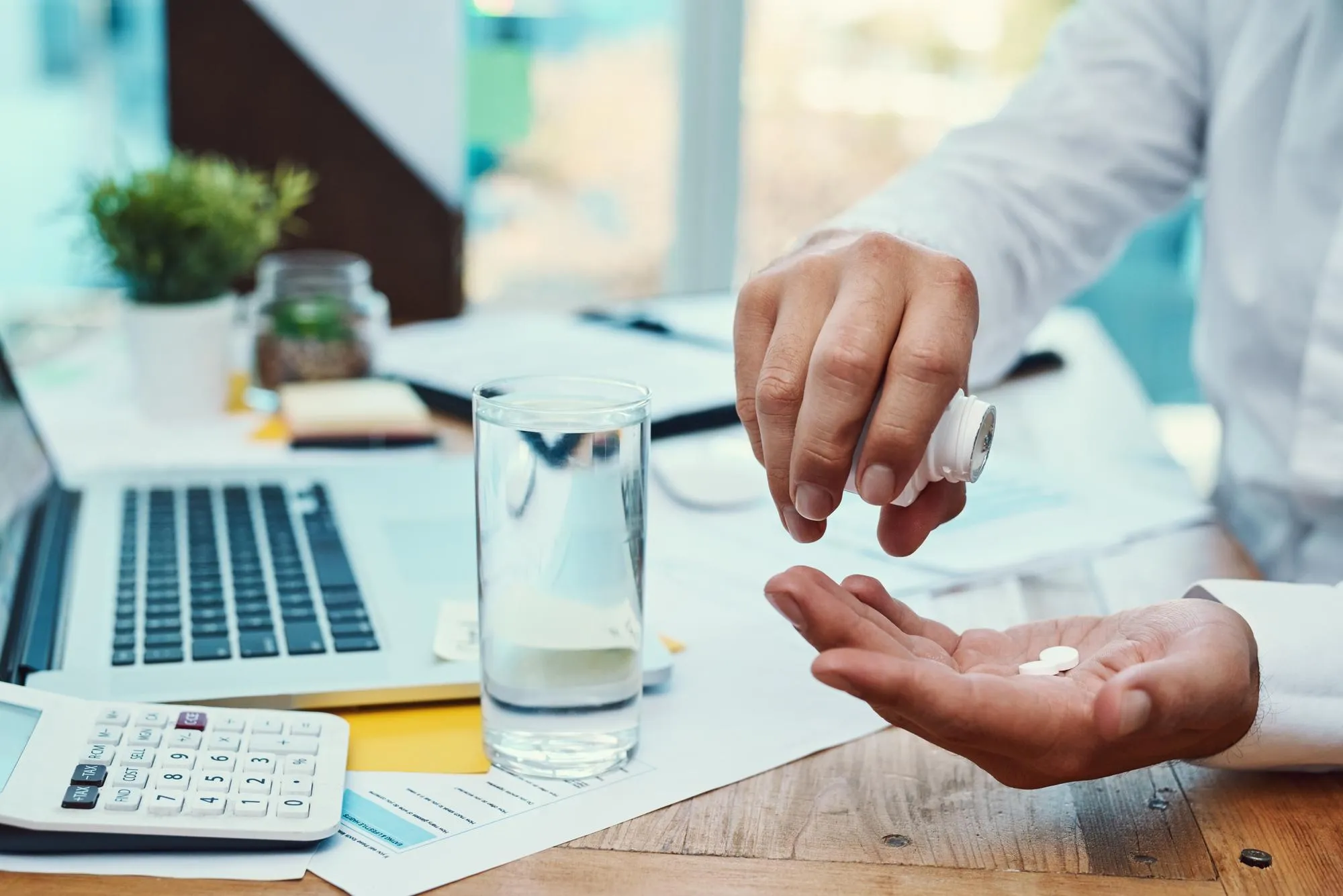 Person taking medication at a desk, symbolizing improved medication access for patients through efficient pharmacy workflows