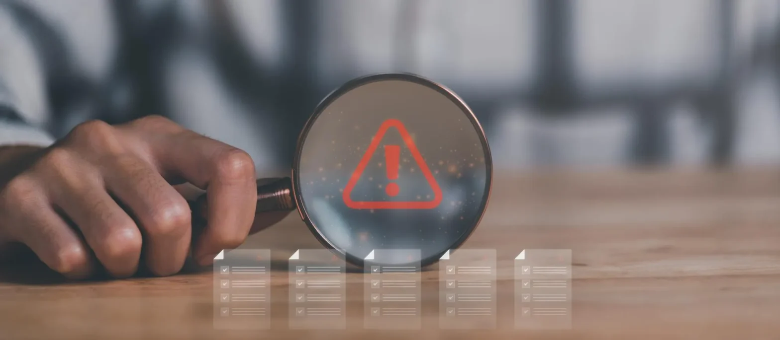 Magnifying glass highlighting an alert icon over documents, representing Prior Authorization Services used to identify and resolve prior authorization denials before prescription delays occur.