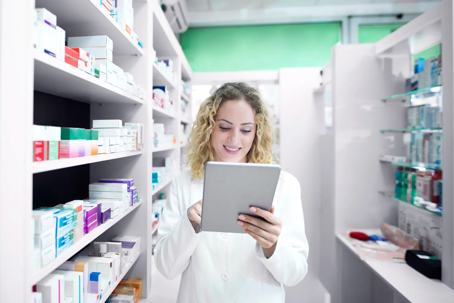 Pharmacist using a tablet to review prescriptions and reduce prior authorization delays in pharmacy workflows.